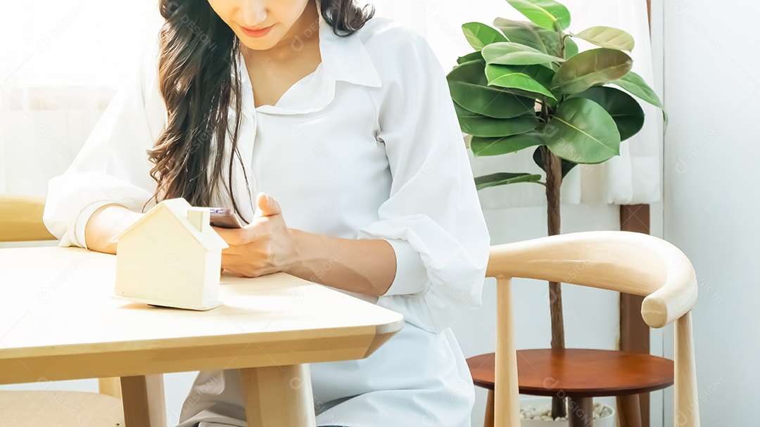 smartphone na mão da mulher e casa modelo