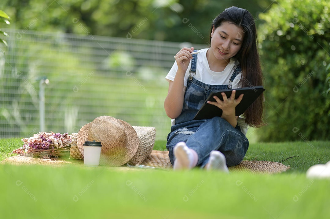 Jovem relaxando no gramado e usando um tablet. Tablet com caneta na mão.