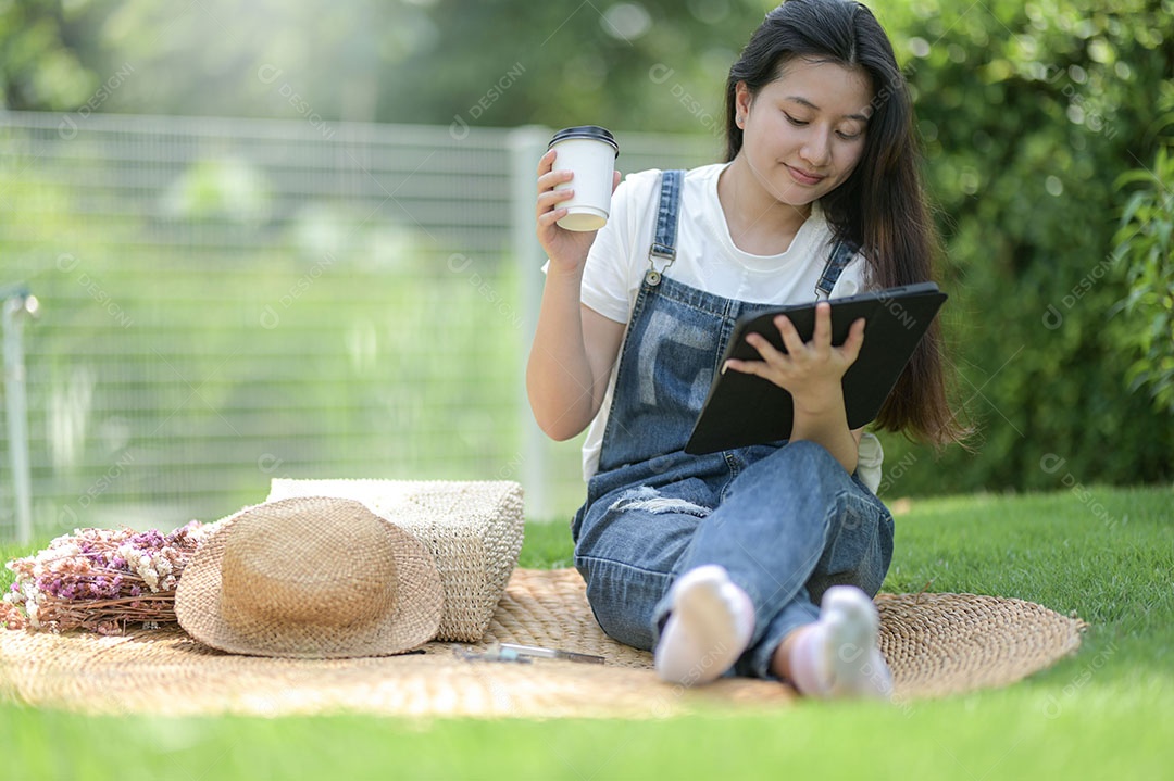 Adolescente senta-se na grama relaxando com um tablet e uma xícara de café, conversando online.