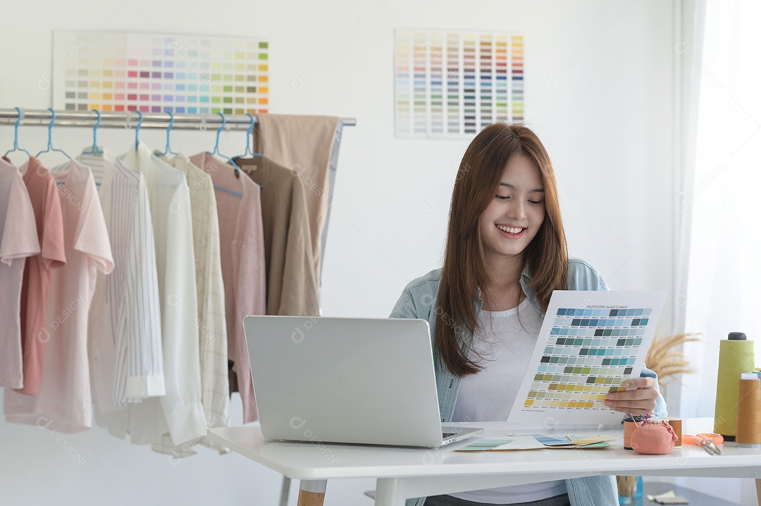 Young woman sews in a designer's workspace with design equipment, laptop and smartphone in a workshop.
