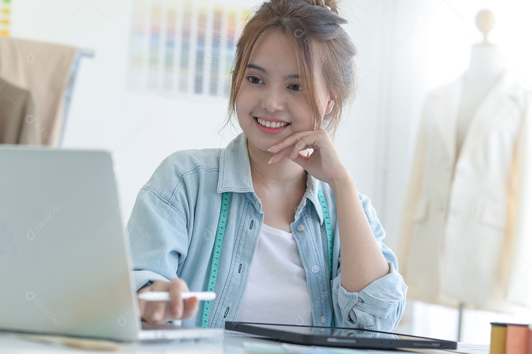 Jovem costura no espaço de trabalho de um designer com equipamento de design, laptop e smartphone em uma oficina.
