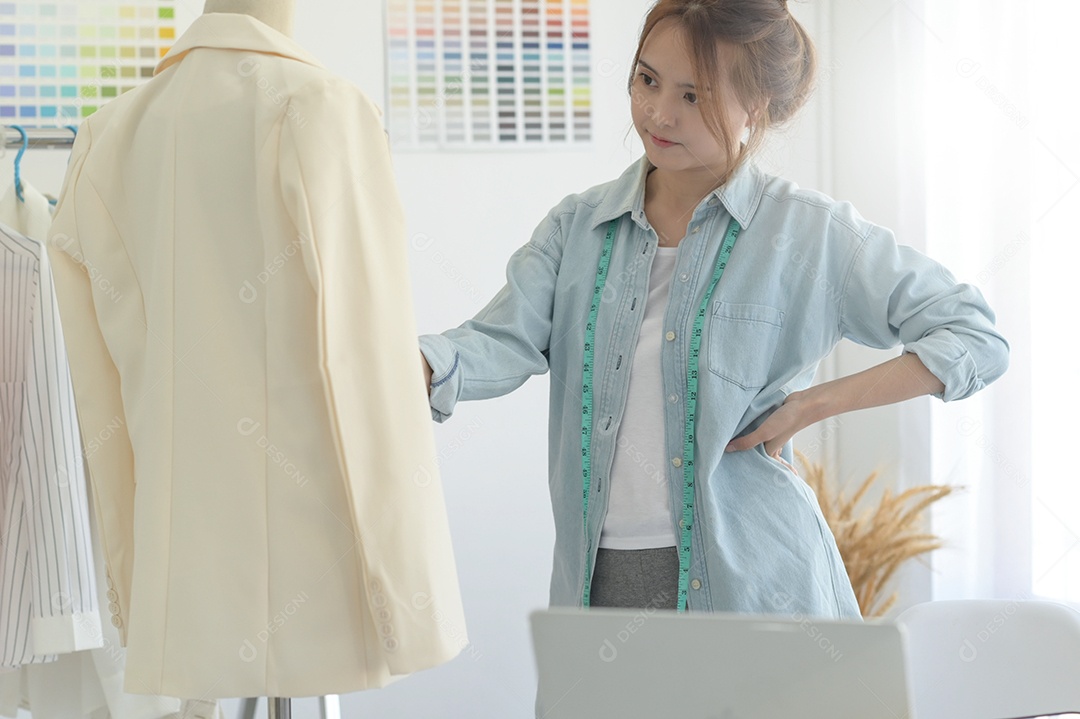 Jovem costura no espaço de trabalho de um designer com equipamento de design, laptop e smartphone em uma oficina.