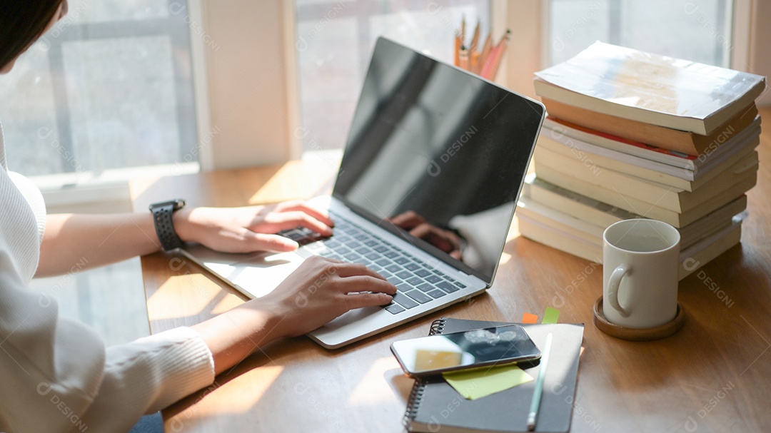 Feche, a mão da jovem está usando um laptop em uma mesa de madeira no escritório com bela iluminação.