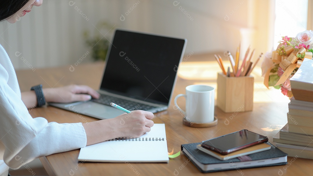 Jovem empresária estão tomando notas e usando um laptop de tela em branco em um escritório moderno.