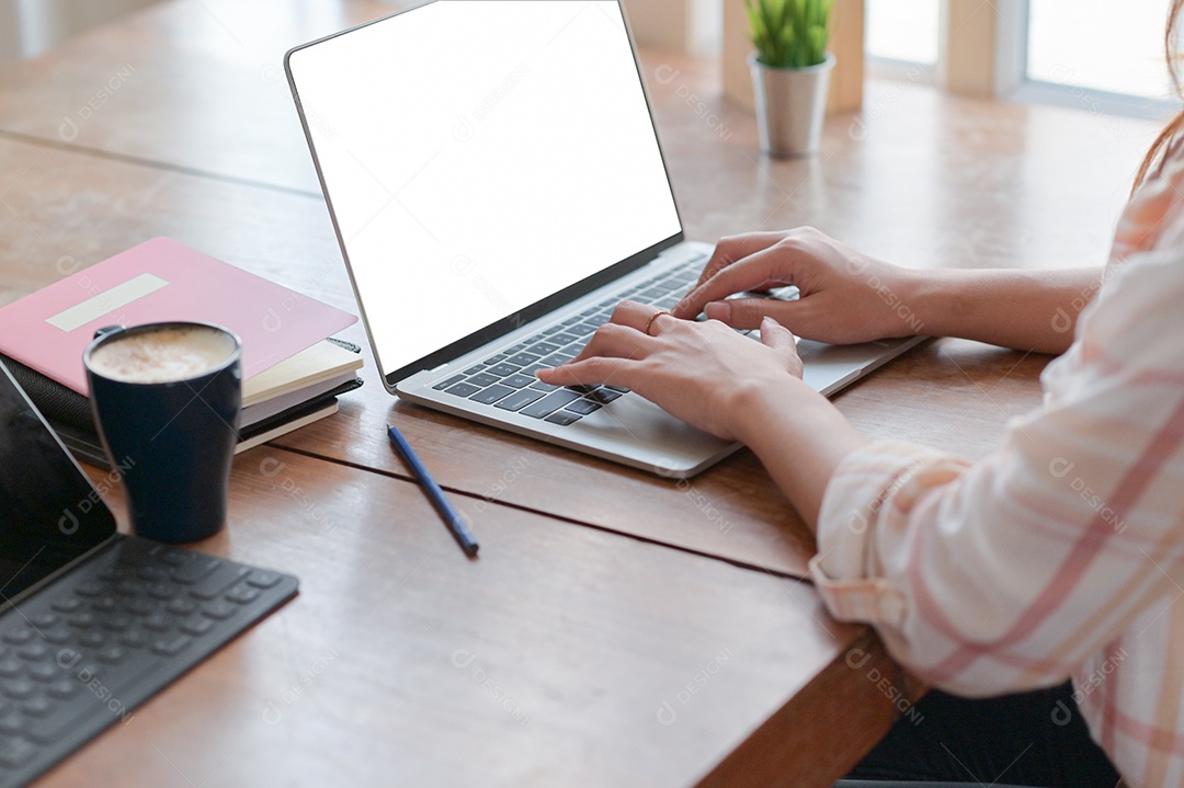 Vista da mão da mulher de negócios está usando um laptop em uma mesa com café no escritório confortável.