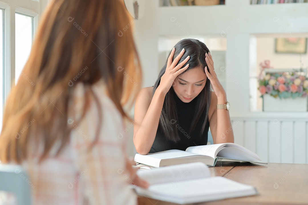 Foto recortada de duas alunas asiáticas estão lendo muito para se preparar para estudos universitários.