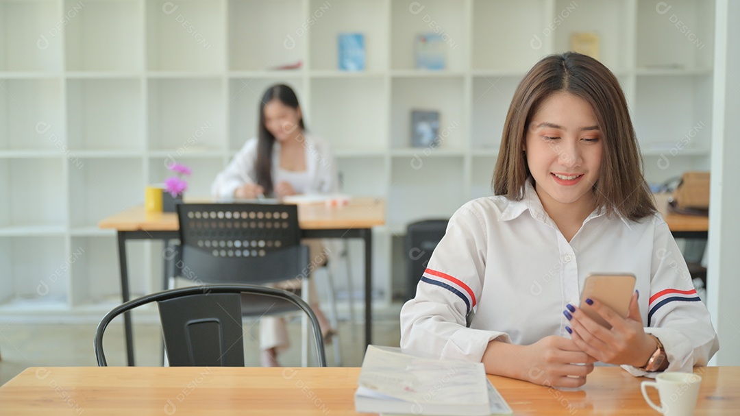Retrato de uma jovem mulher vestindo uma camisa branca está usando um smartphone no escritório contemporâneo... Na parte de trás havia outra garota sentada.