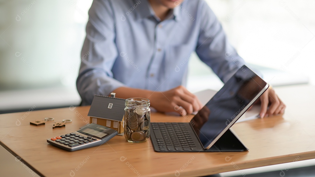 Laptop, moeda em uma garrafa de vidro, calculadora com uma casa modelo na mesa e um fundo desfocado pessoas