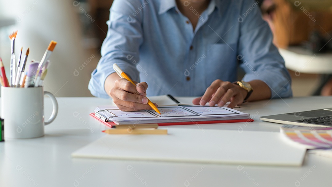 Foto recortada do Designer está desenhando uma tela de smartphone para futuros clientes na mesa com laptop e artigos de papelaria.