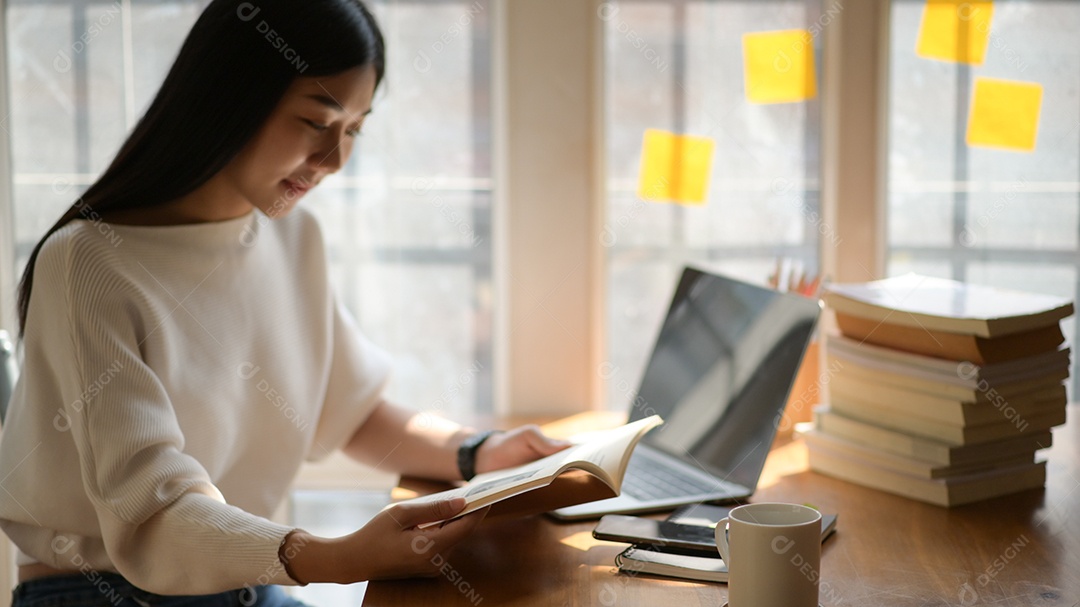 Foto recortada de uma adolescente asiática lendo um livro para se preparar para os exames de admissão da universidade.