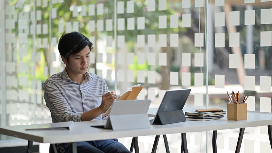Foto recortada de um estudante asiático do sexo masculino com um laptop e estacionário se preparando para concluir sua tese para terminar a universidade.