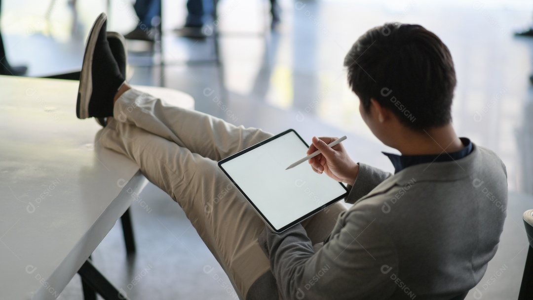 Foto recortada de um jovem empresário usando um tablet. Ele se sentou em uma cadeira e seus pés repousaram sobre a mesa.