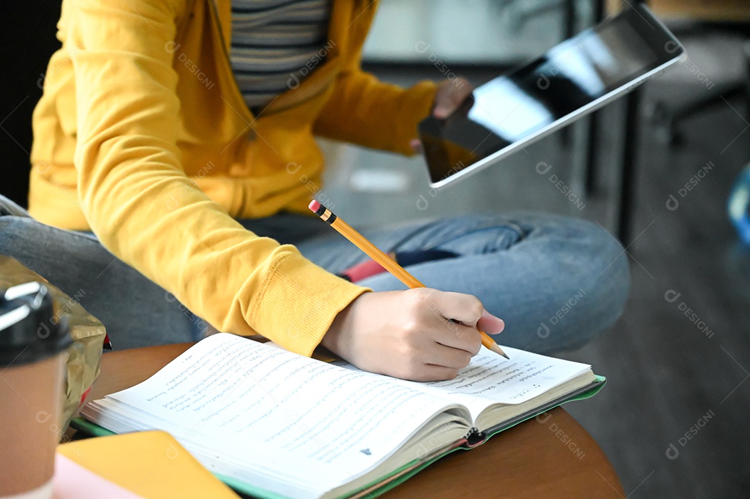 Foto recortada de uma jovem aluna tomando notas e usando um laptop, preparando-se para o exame de admissão.