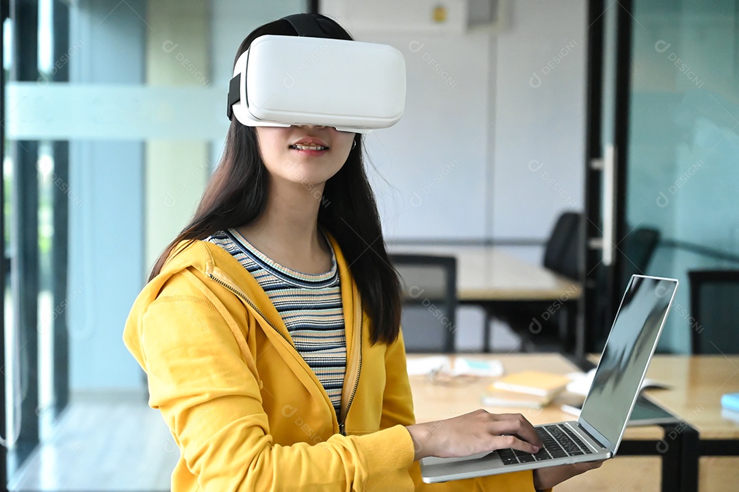 Foto recortada de uma jovem estudante usando óculos VR e usando um laptop.
