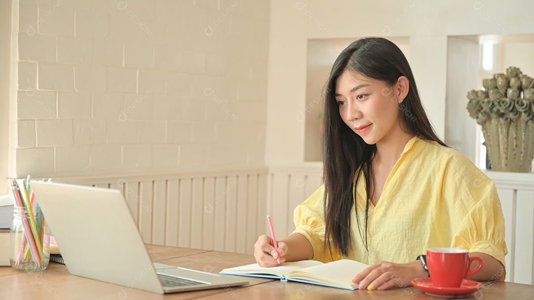Jovem asiática trabalham em casa para se proteger contra o coronavírus. Ela se encontra por videoconferência e faz anotações