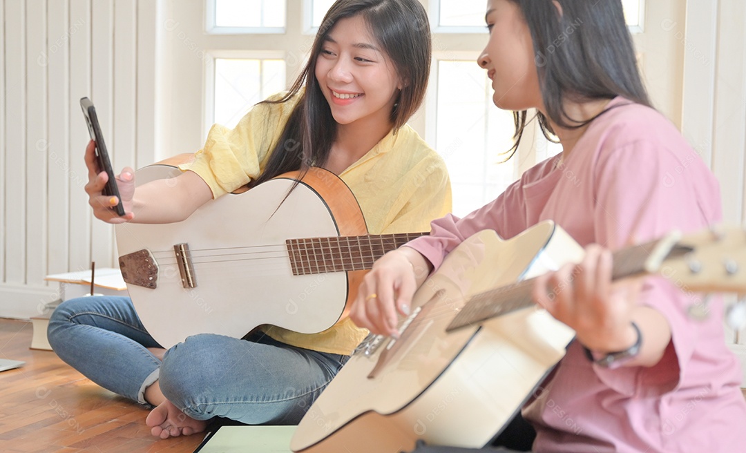 Foto recortada de adolescentes e amigos tocando violão e usando uma chamada de vídeo para smartphone. Eles ficam em casa durante a contenção do vírus Covid-19.