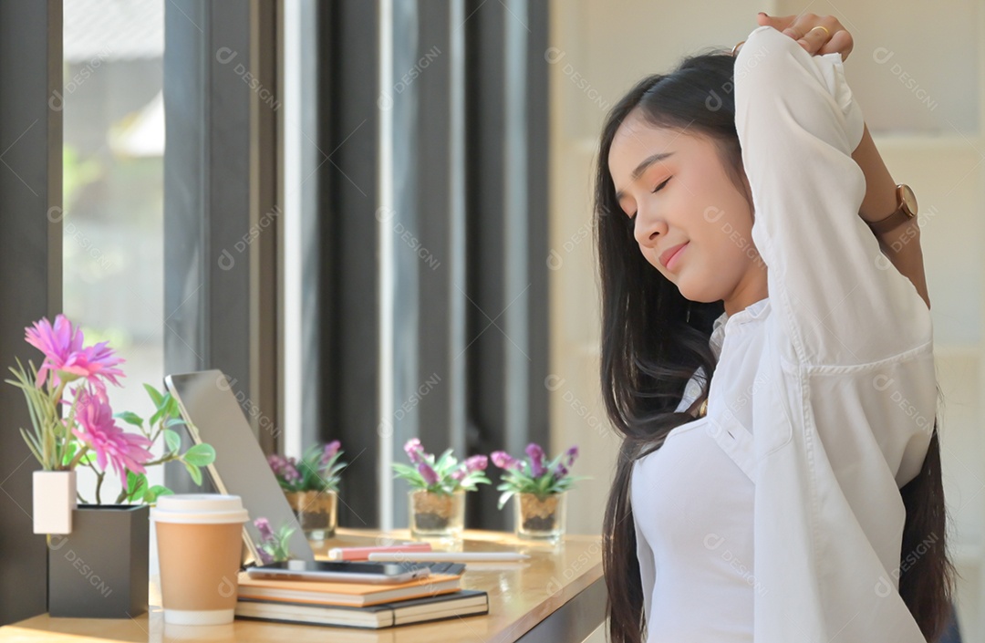 Mulher asiática sentam-se no espaço de trabalho e esticam os braços para relaxar durante uma reunião online com um laptop.