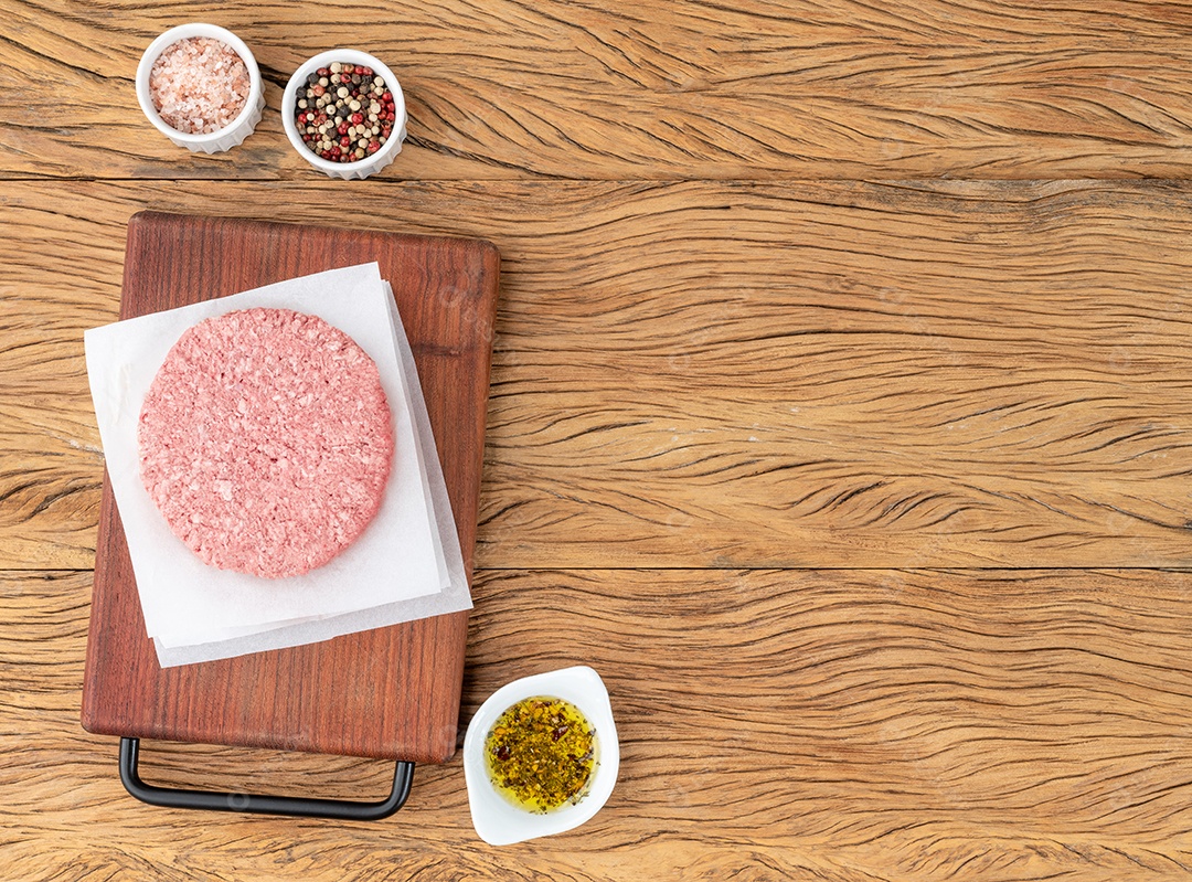 Hambúrguer de carne crua sobre placa de madeira com temperos e espaço de cópia.