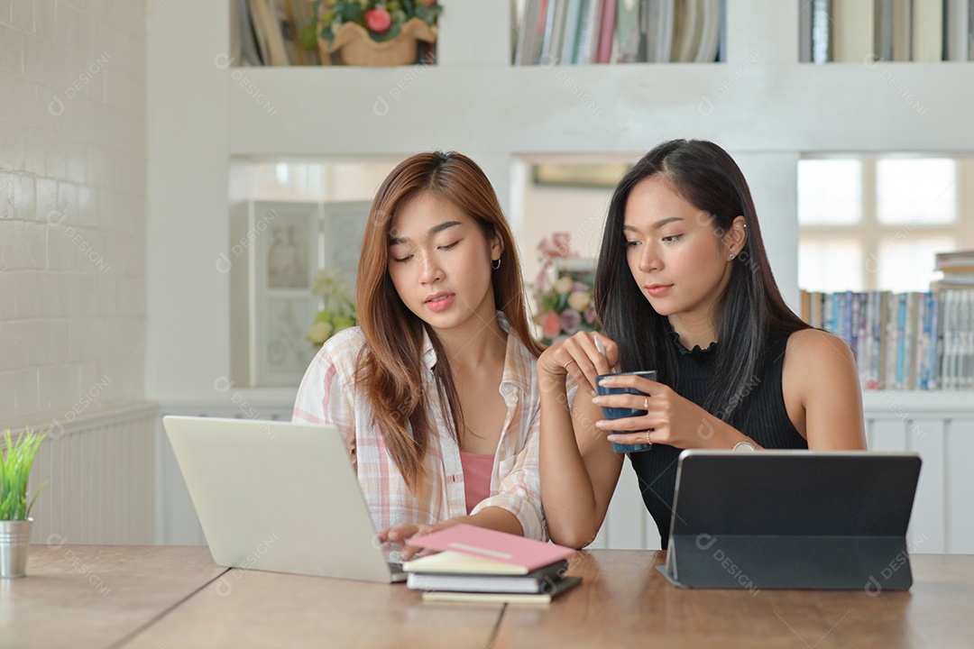 Two young female students with coffee are using a laptop to study online at home in the summer semester, Work from home, Work from home.
