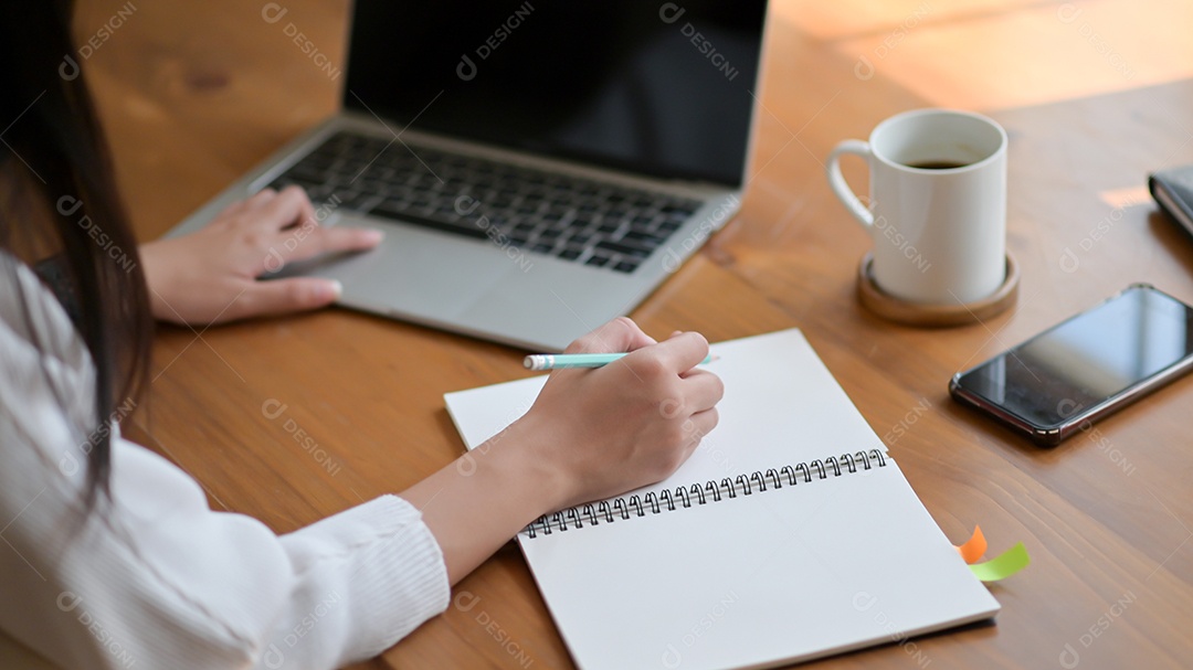 Jovem está usando um laptop e escrevendo um relatório. Ela trabalha em casa.