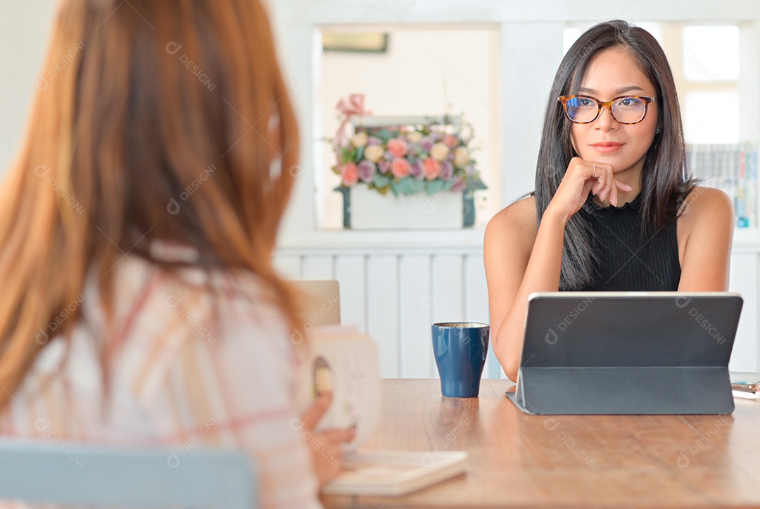 Duas mulheres conversando com um tablet na sala de estar. Eles se sentam espaçados para evitar o vírus.