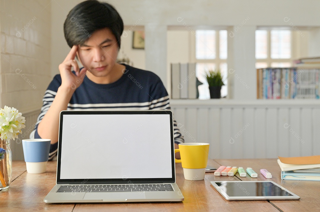 Laptop e um smartphone colocados na mesa e o jovem está sentado para trabalhar na parte de trás.