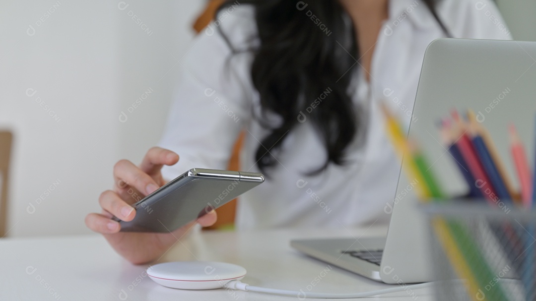 Menina está colocando o smartphone no carregador sem fio com o laptop na mesa.