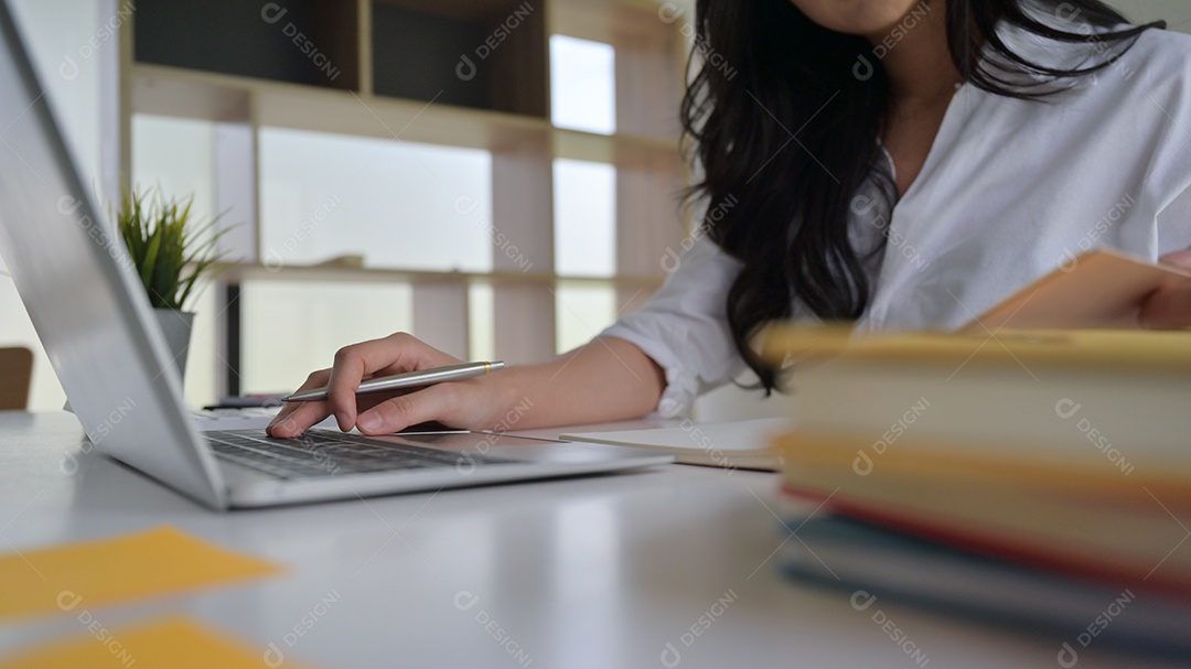 Menina segurando uma caneta na mão em um teclado de laptop. Ela está trabalhando em um escritório moderno.