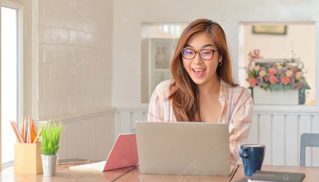 Mulher de óculos está usando um laptop e sorrindo alegremente.