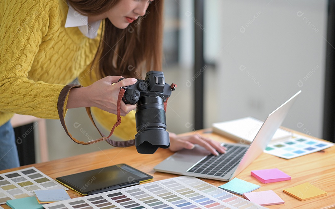Designers estão olhando para fotos de câmeras e usando um laptop.