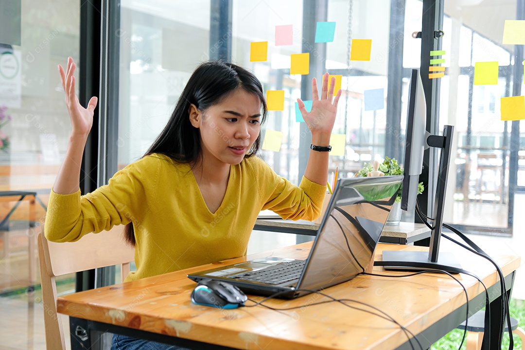 Mulher asiática veste uma camisa amarela, olha para a tela do laptop e mostra uma maneira séria. Conceitos de investimento, conceitos de programador.