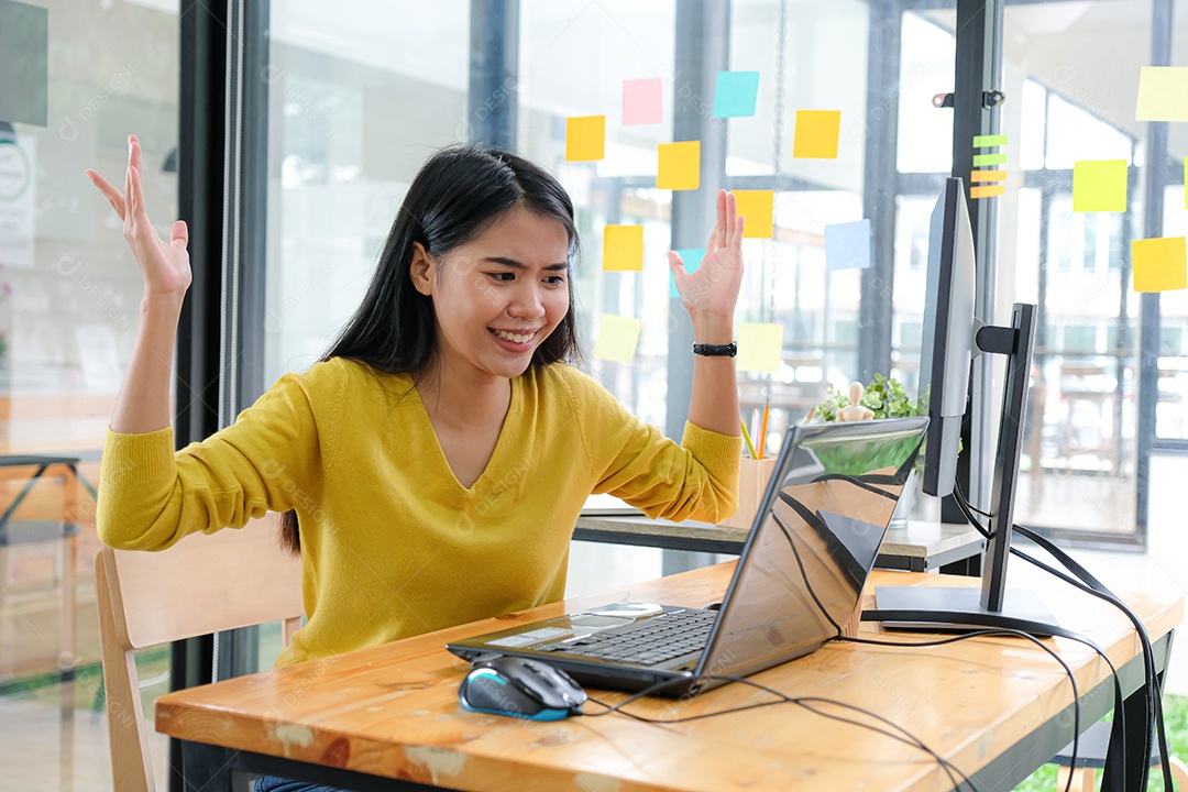 Mulher asiática usava uma camisa amarela, olhou para a tela do laptop e parecia feliz. Conceitos de investimento, conceitos de programador.