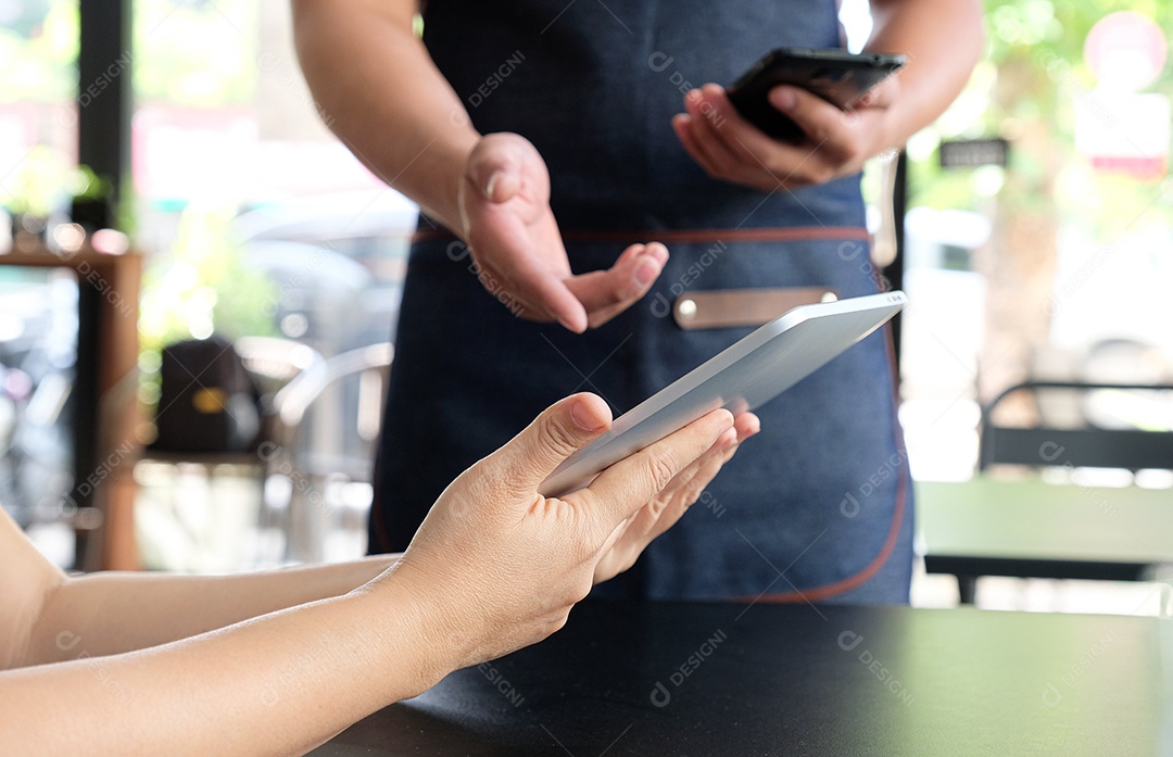 Funcionário segurando um smartphone para salvar o menu do pedido do cliente. O cliente vê o menu do tablet.