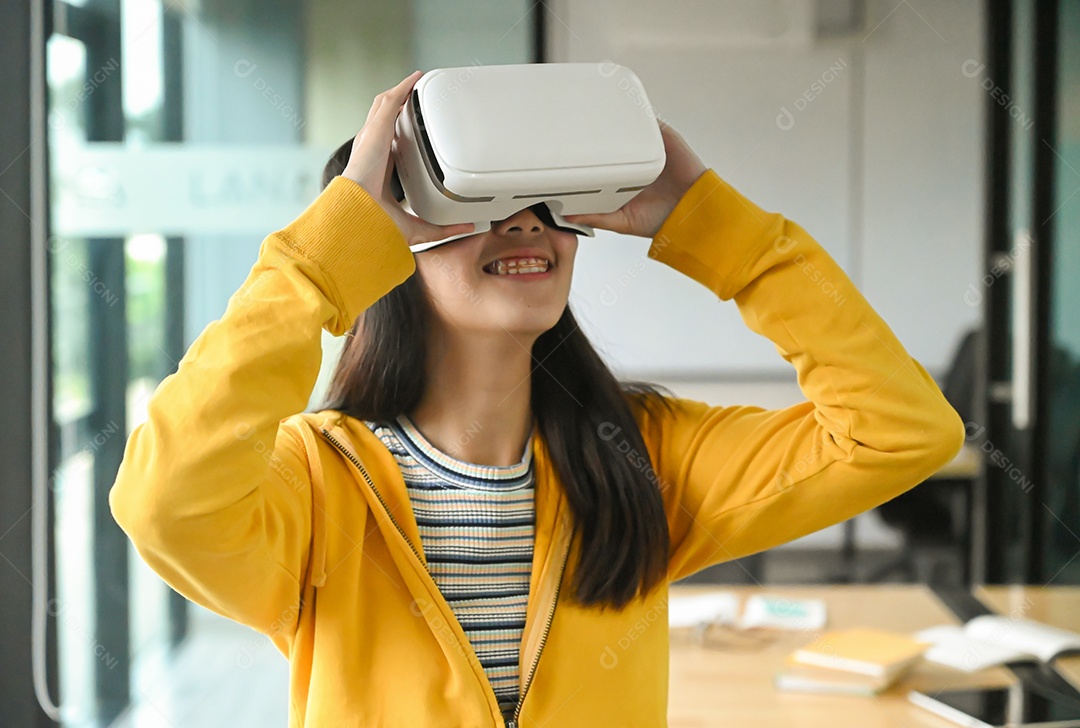 Menina asiática vestindo uma camisa amarela está usando o fone de ouvido VR. Ela está sorrindo.