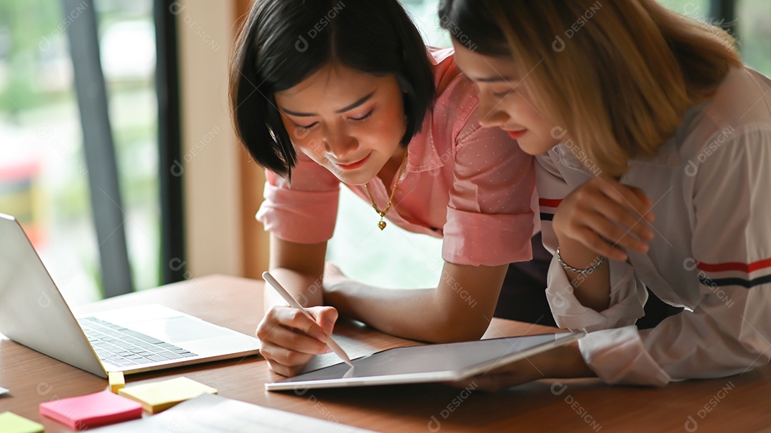 Designer gráfico feminino asiáticas trabalhando juntos no escritório Eles usam laptop e tablet.