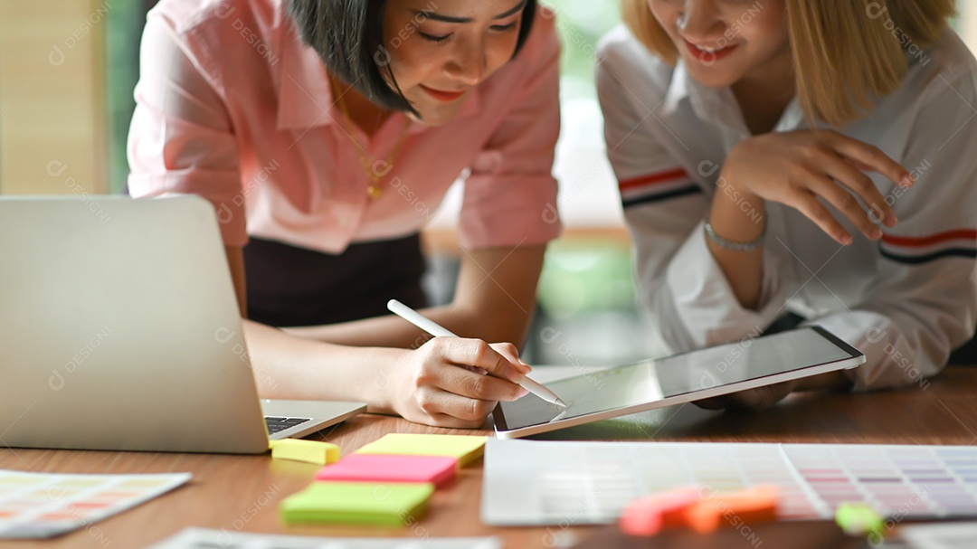Designer gráfico feminino asiáticas trabalhando juntos no escritório Eles usam laptop e tablet.