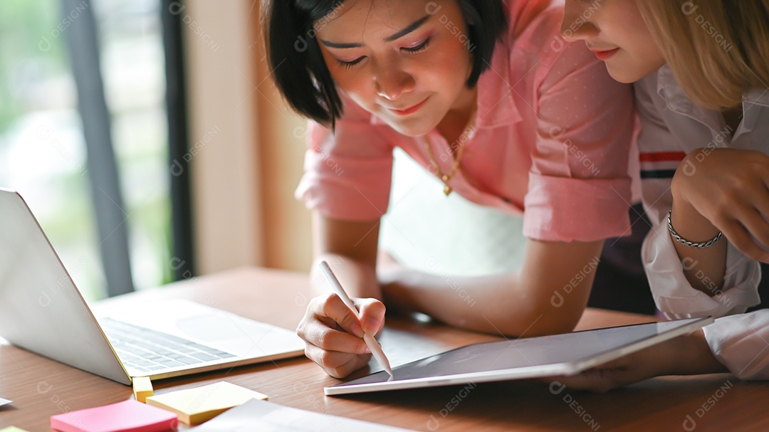 Designer gráfico feminino asiáticas trabalhando juntos no escritório Eles usam laptop e tablet.