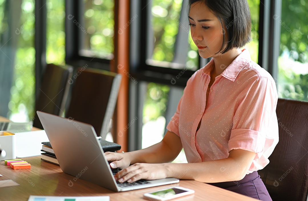 Mulher adolescente asiática está usando um laptop no escritório.