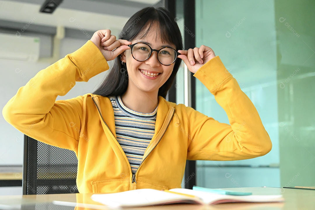 Aluna asiática com óculos e sorriu para a câmera. Ela está lendo livros de preparação para exames.
