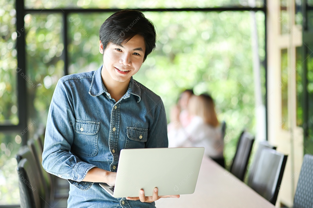 Homem de negócios jovem está segurando um laptop no escritório.