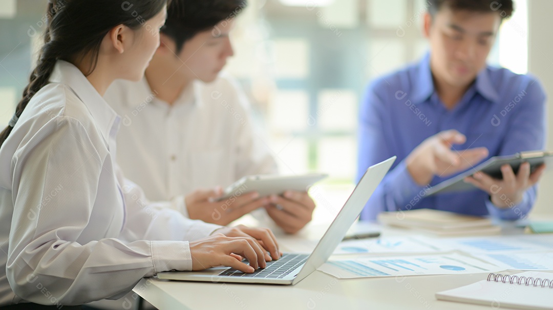 Jovens profissionais planejam uma estratégia para um novo projeto Enquanto a secretária usa o laptop e analisa os dados dos gráficos.