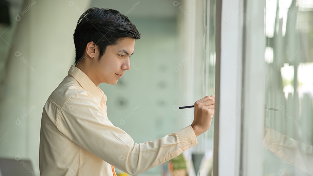 Homem de negócios jovem está tomando notas trabalhando em uma nota em uma parede de vidro em um escritório moderno.