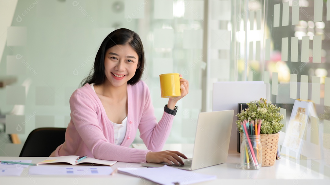 Jovem bsinesswoman planejando para o próximo ano no escritório moderno, ela segura uma xícara de café e olha para a câmera.