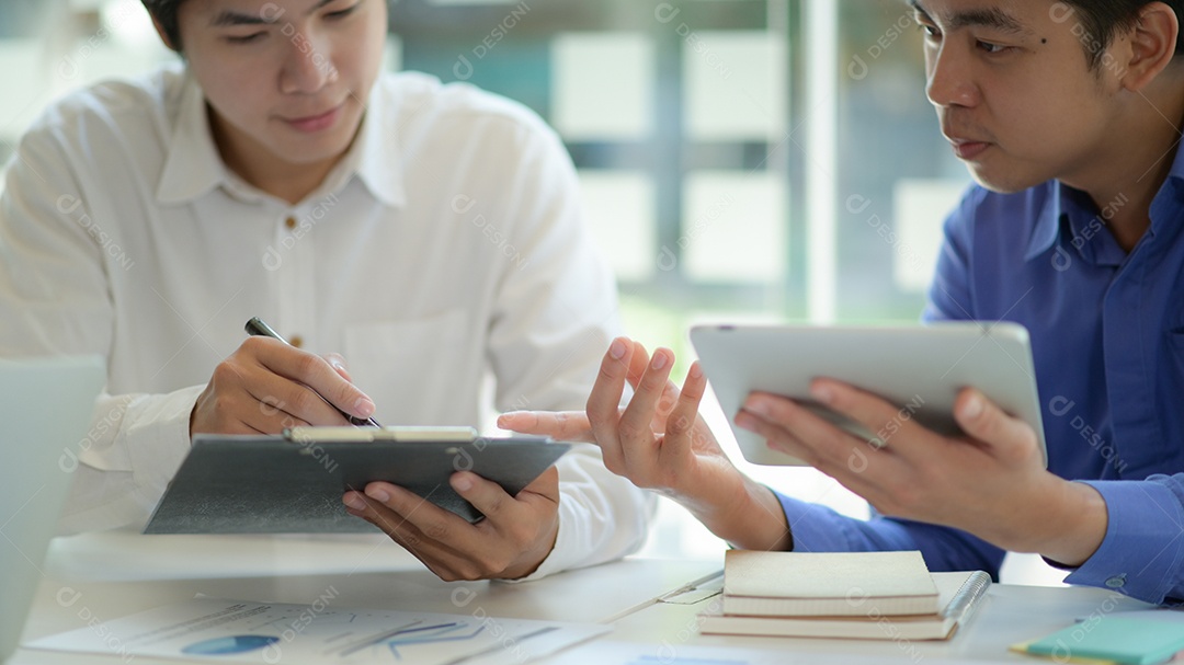 Parceiros de negócios falam sobre o projeto com tablets e gráficos na sala de reuniões.