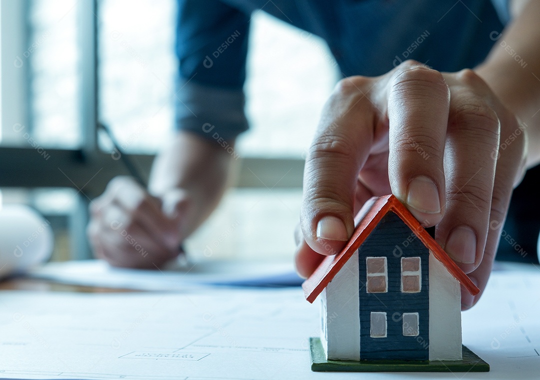 Jovem aquitetos estão elaborando uma planta de casa para apresentar o projeto. Ele pegou a casa modelo na frente, foco na mão e casa modelo.