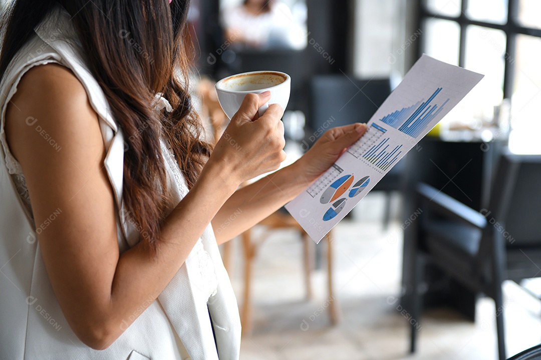 Executivos femininos bebem café e mantêm gráficos disponíveis. Ela estava no escritório.