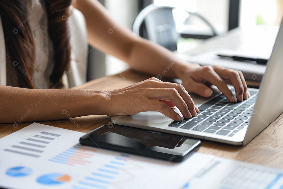 Executivos do sexo feminino estão usando laptops na mesa no escritório. Smartphone colocado no documento gráfico.