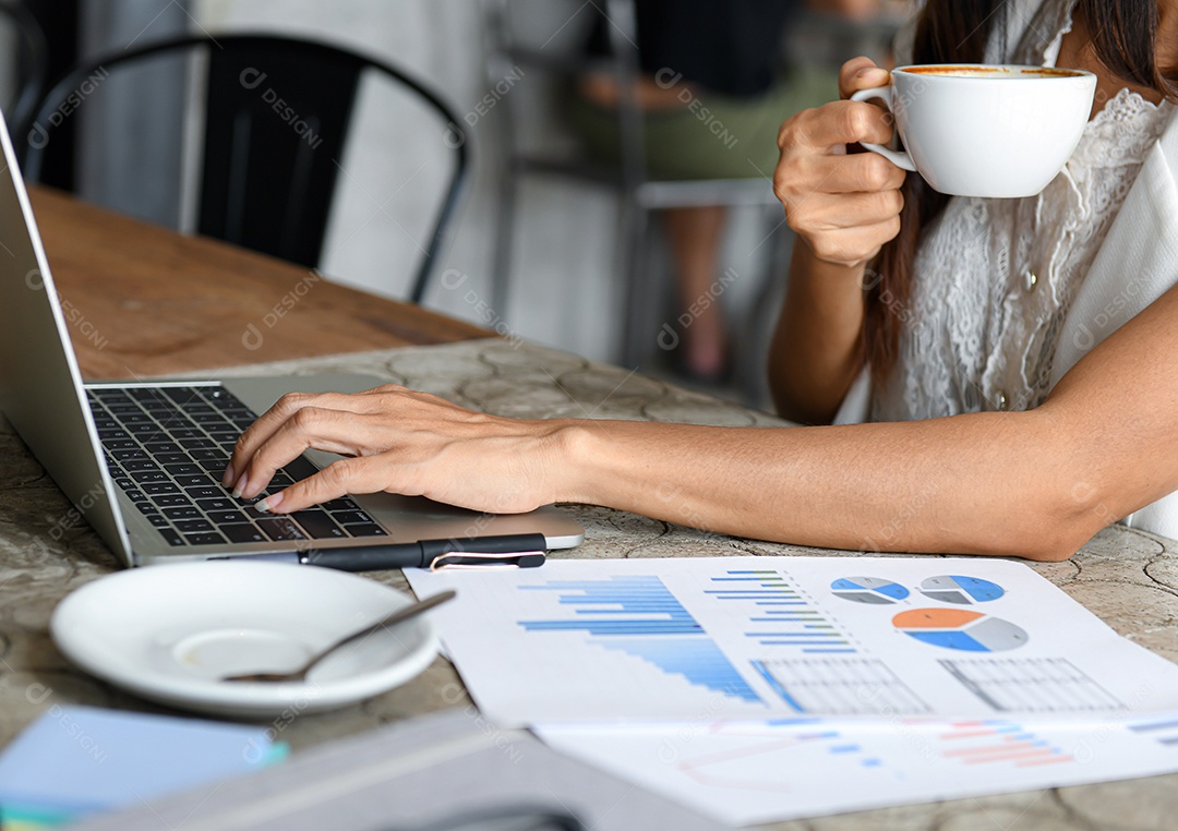 Empresário femininos estão tomando café e usando laptop. Ela trabalha entre o freio de café, gráficos na mesa.