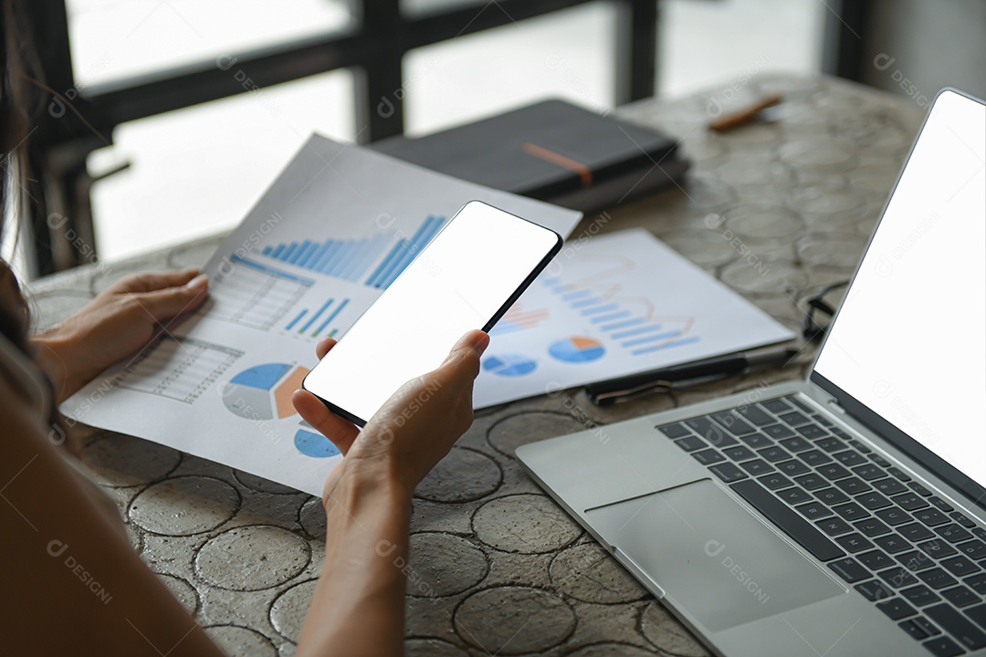 Mão de uma mulher de negócios está usando um telefone celular para encontrar informações. Ela mantém o gráfico e o smartphone na mão.