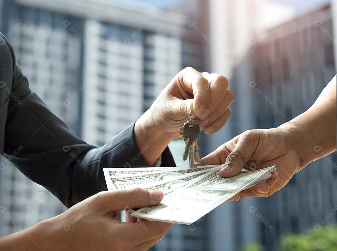 Negociação imobiliária, as pessoas da mão estão pagando o dólar com a outra mão segura as chaves, o fundo é uma imagem de condomínio desfocada.